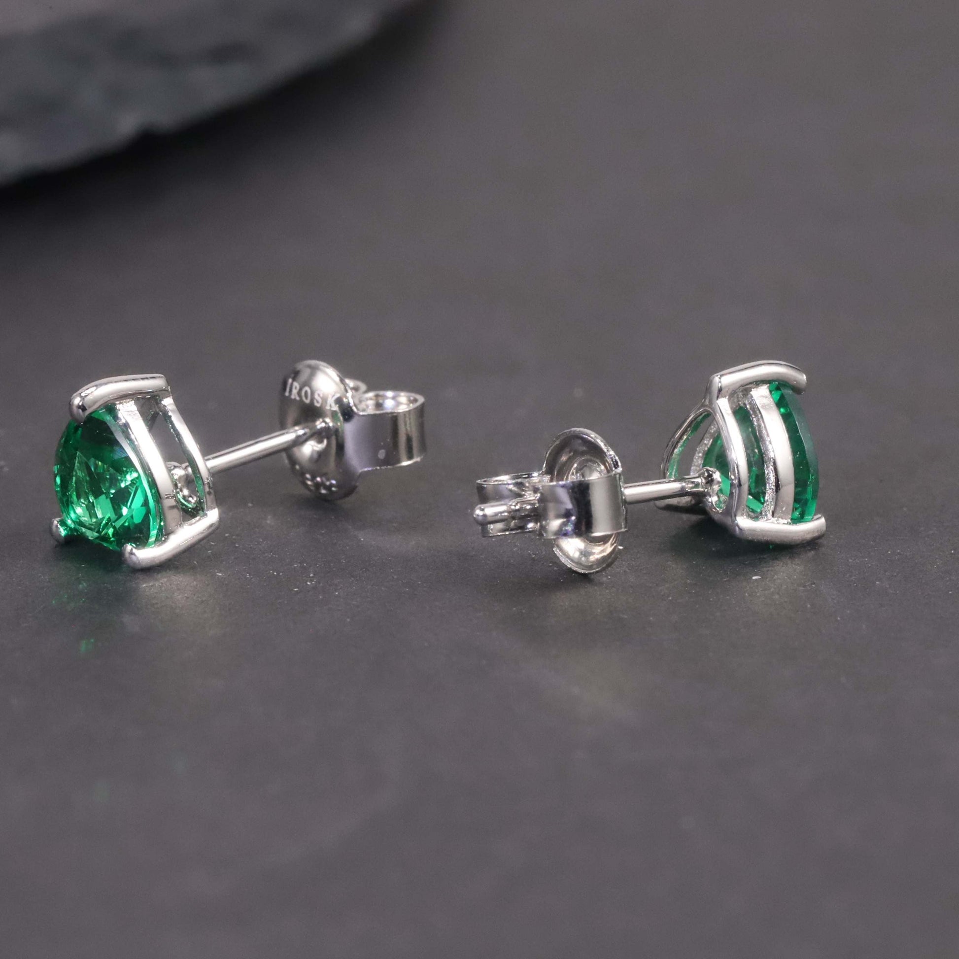 Side view of silver emerald simple heart shape stud earrings on dark background