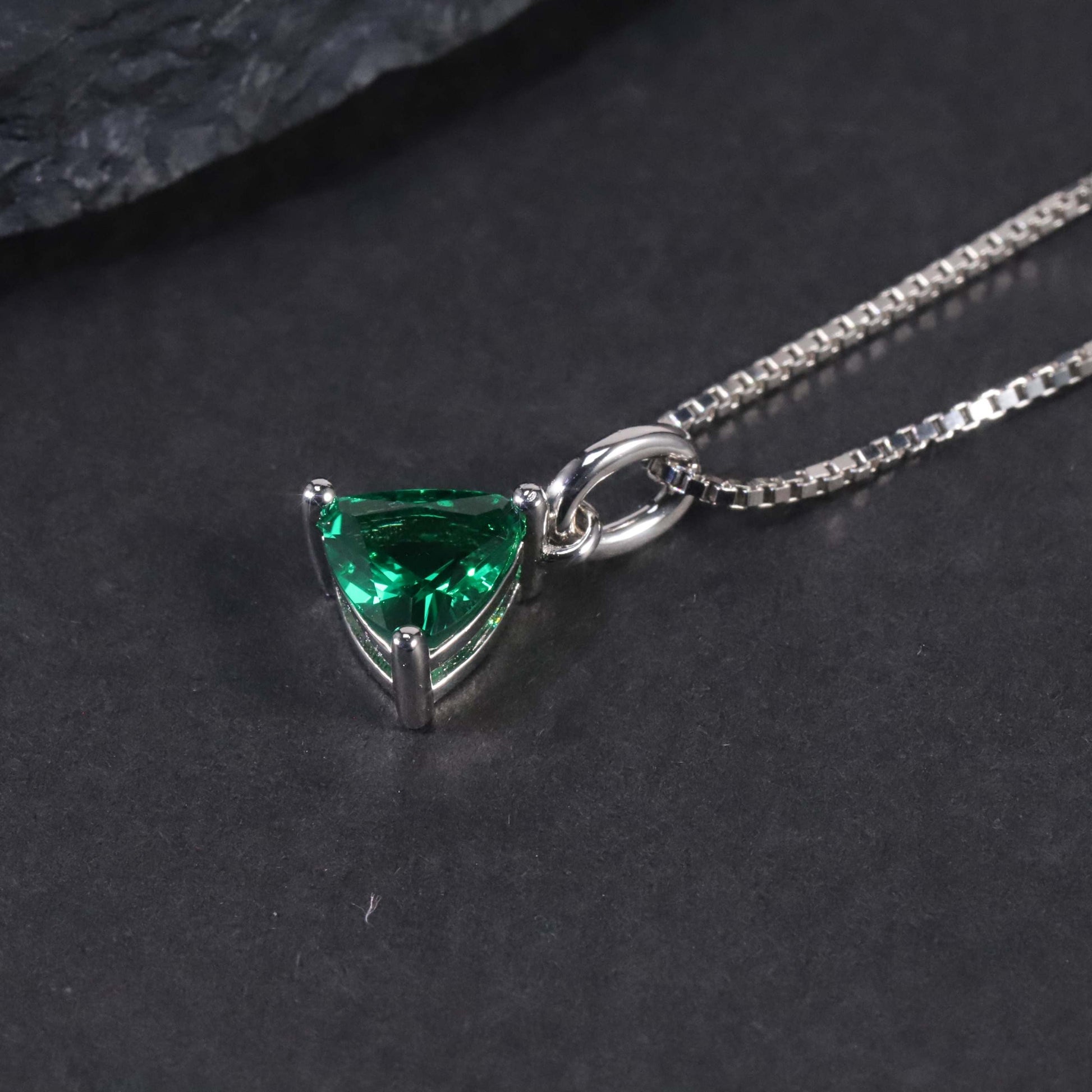 Side view of silver trillion cut emerald pendant on dark background